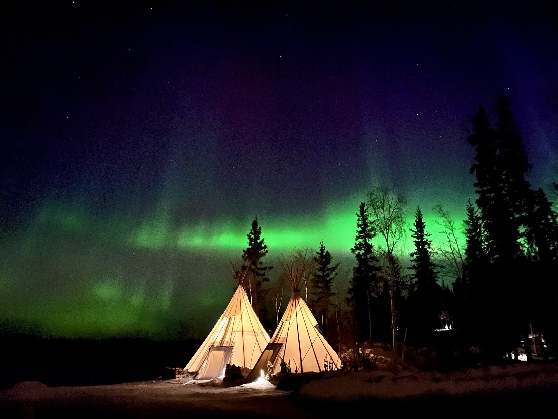Aurora over lit teepees near Yellowknife, Canada