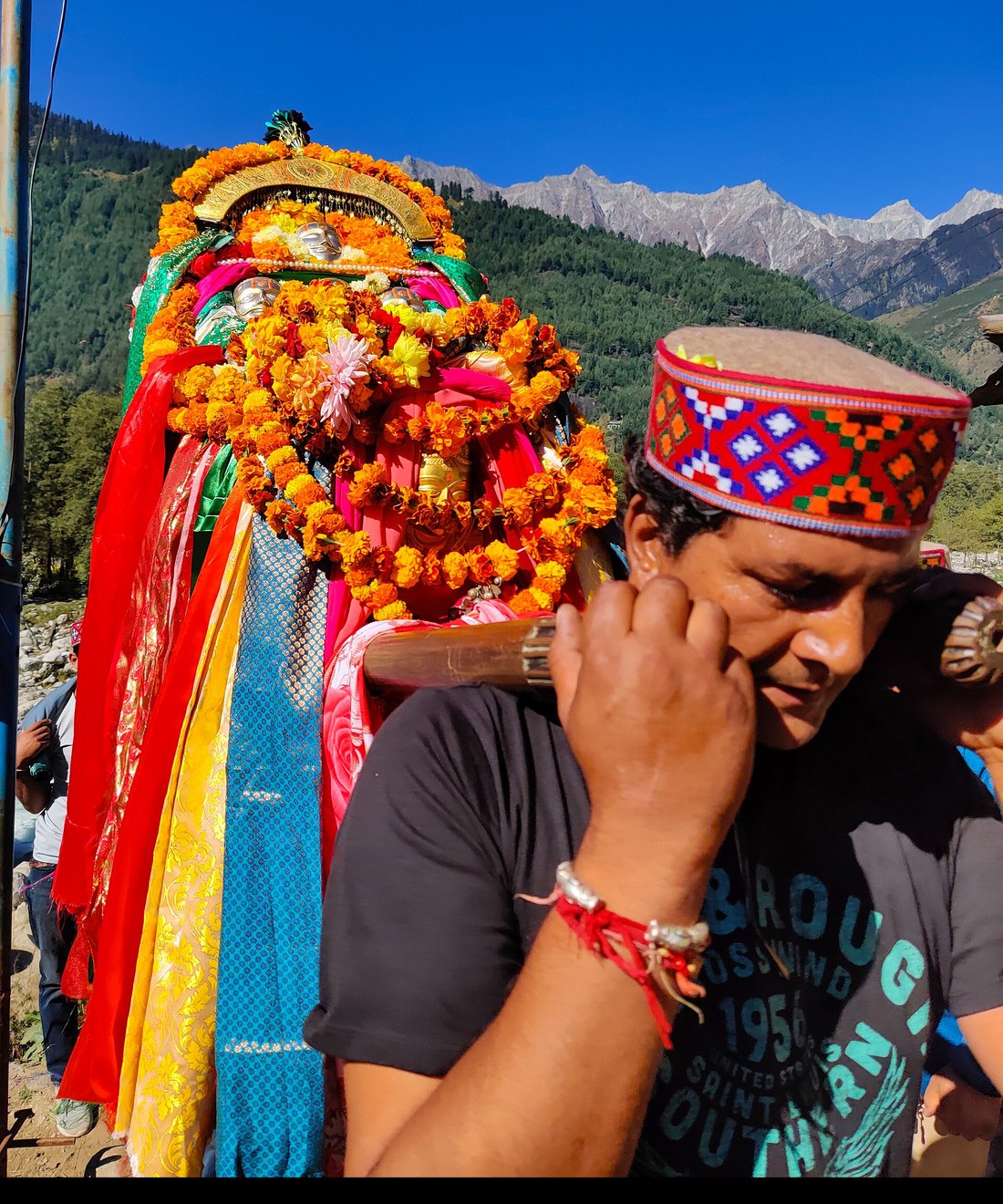 Bearer in a Kullu cap carrying a devta palanquin draped in silk and marigolds
