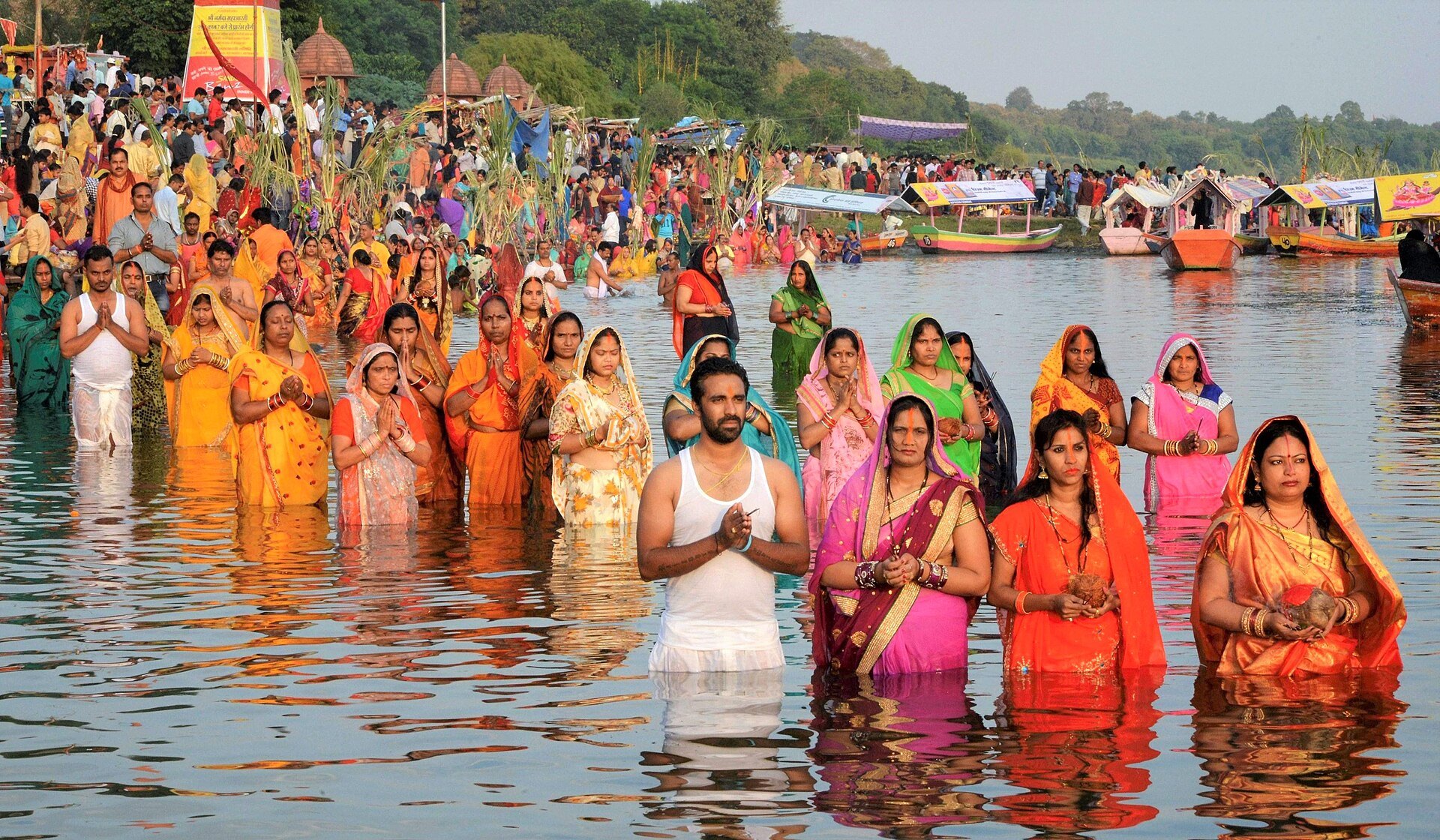 Chhath Puja vratis standing waist deep in the river at sunset holding soop baskets