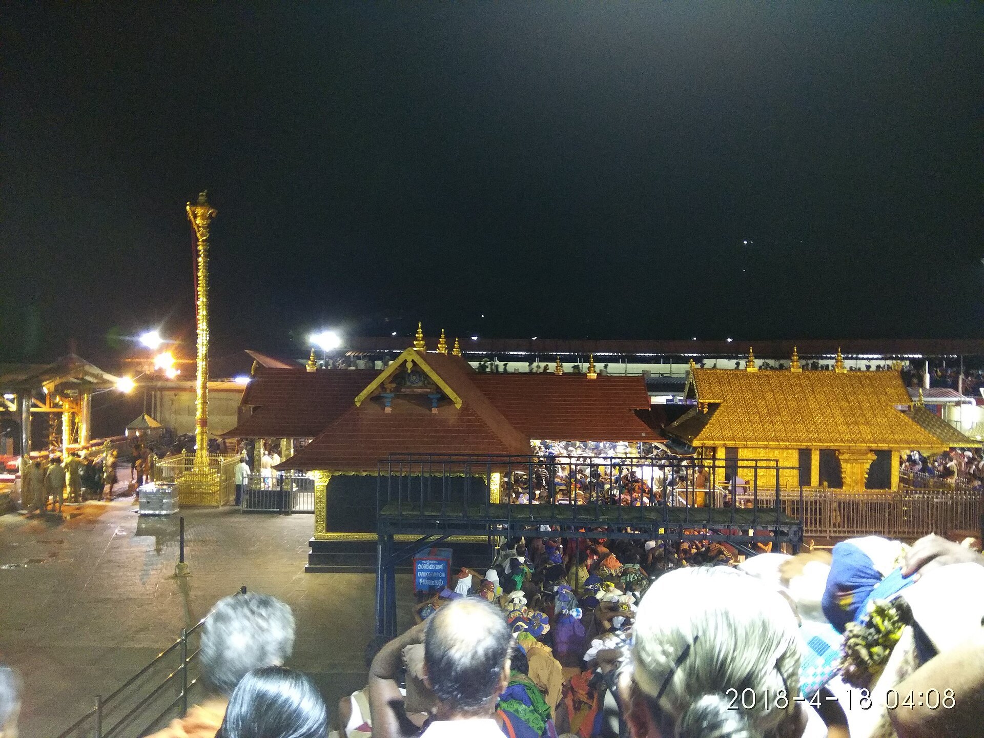 Sabarimala Sannidhanam lit up at night with the golden sanctum roof and pilgrims queued for darshan